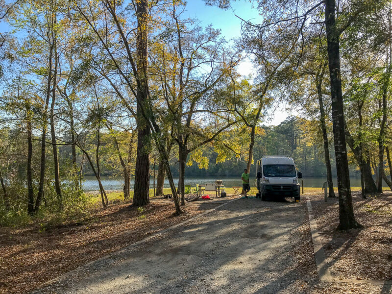a white van is parked at a wooded campsite by the water