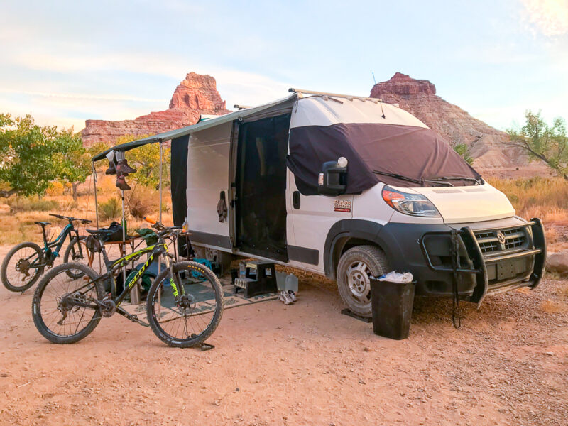 A campervan is parked in a desert landscape with shades and two mountain bikes outside