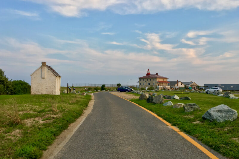 a road lined with historic structures including a lighthouse under a blue sky