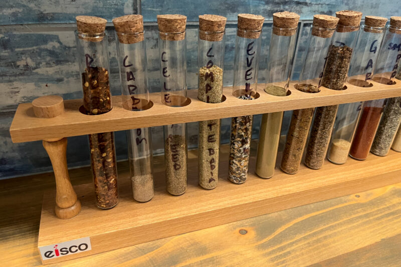 A wooden test tube rack with glass cork-topped test tubes filled with spices