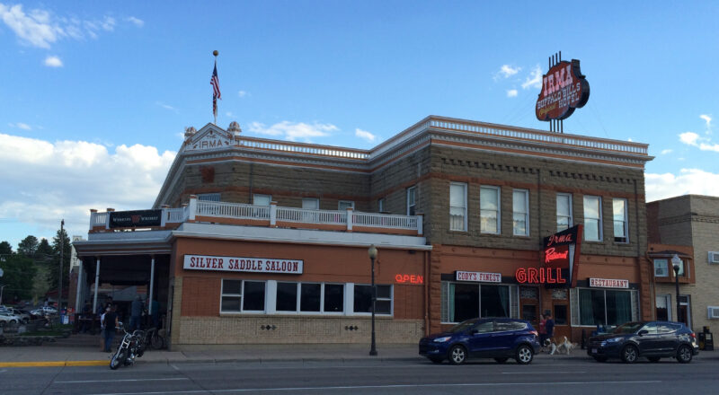 the irma hotel and silver saddle saloon, a small beige brick building with cars and motorcycles parked out front
