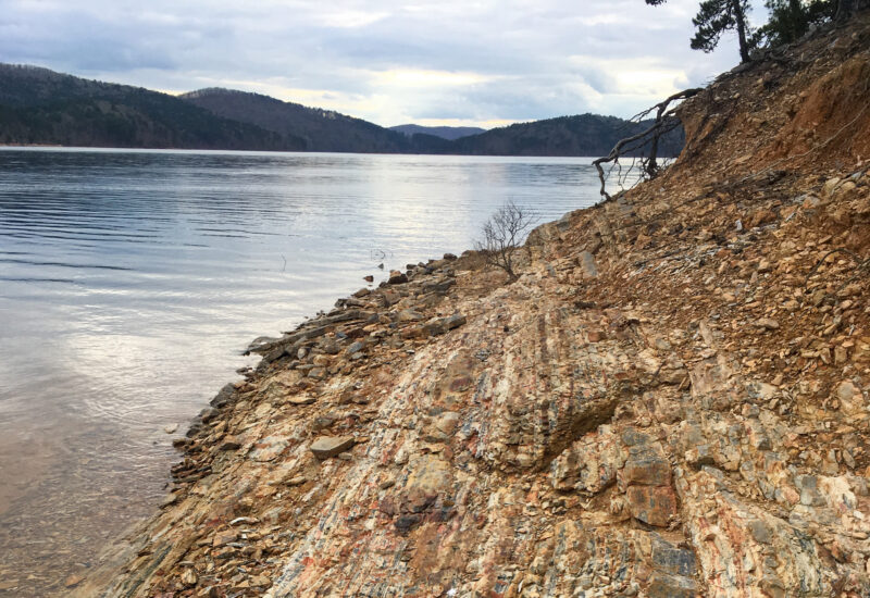 the rocky shore of a lake with hills in the background