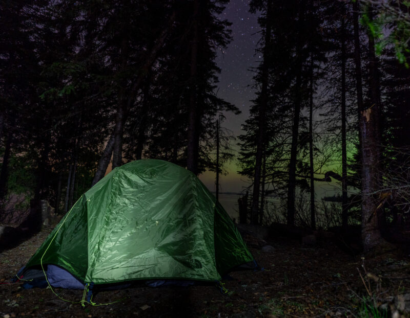 a tent pitched at a campsite at night with the northern lights in the sky