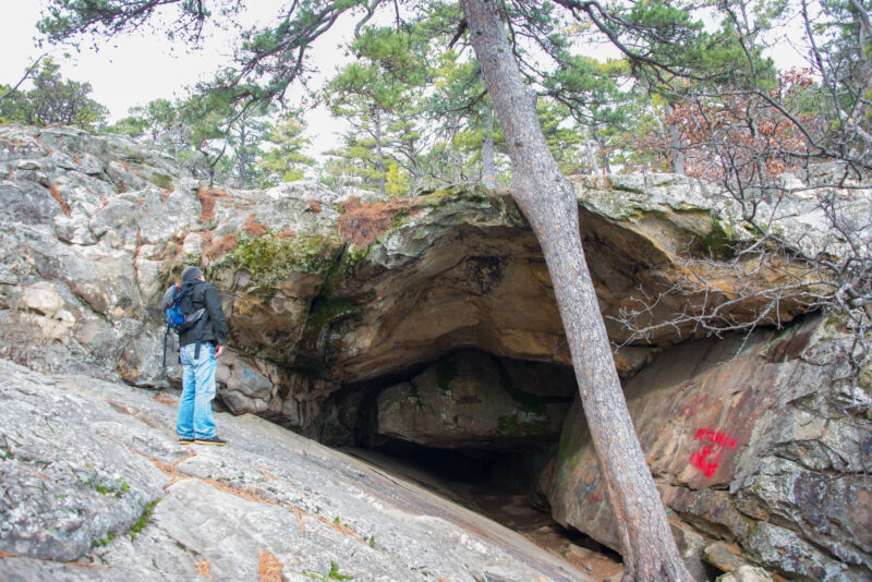 a backpacker stands at the entrance to a rock cave