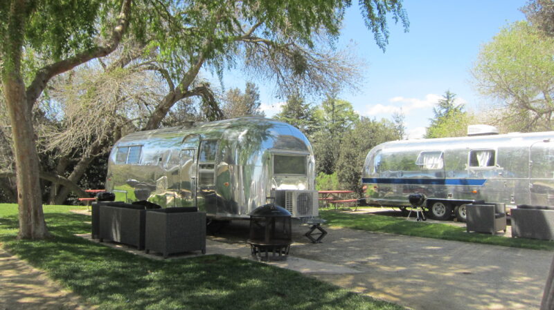 two shiny silver airstream trailers are parked at a campground
