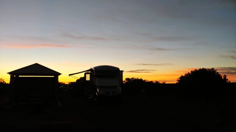 a campground with an rv in silhouette at sunset under a blue and orange sky
