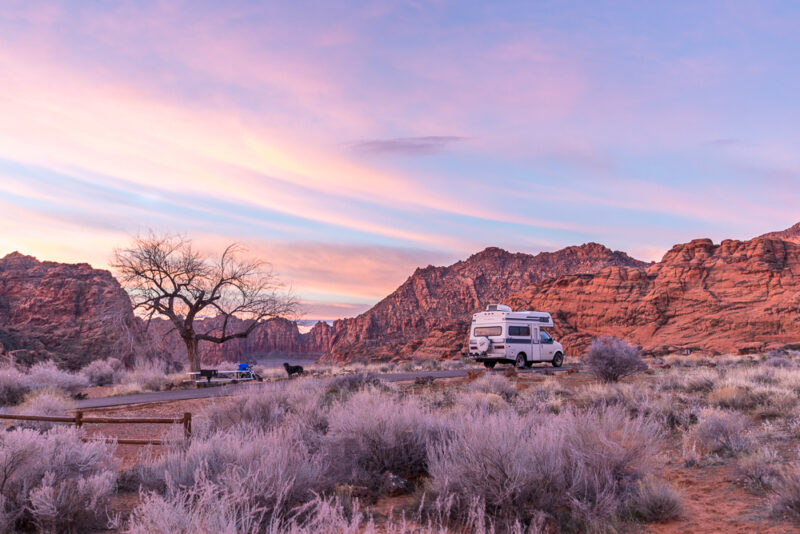 an rv is parked in the desert near red rocks under a pink and blue sunset sky