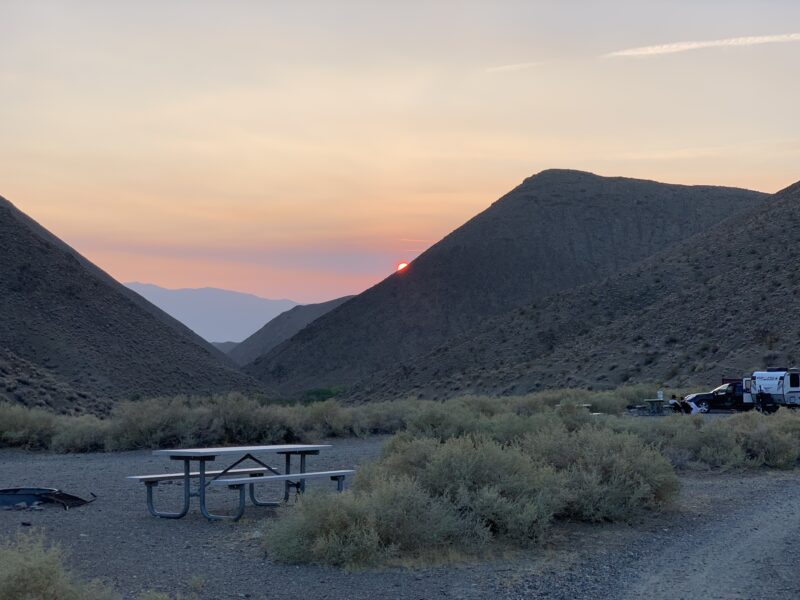 a campsite in the desert with a picnic table at sunset surrounded by mountains