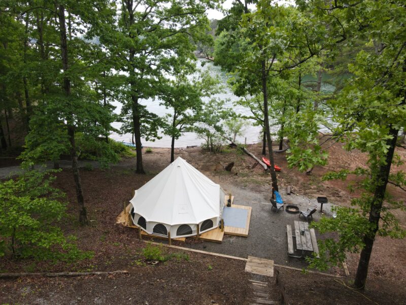 an aerial view of a glamping tent at a wooded campsite by the water