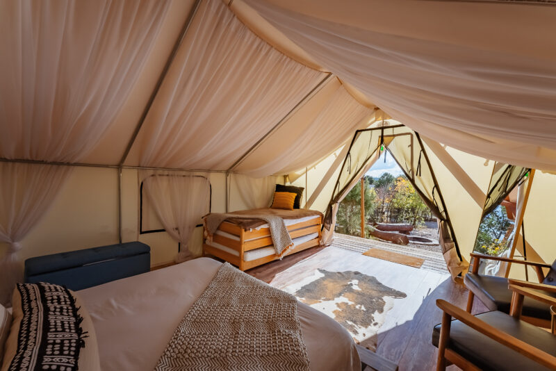 The interior of a glamping tent depicts multiple beds with a view into nature.
