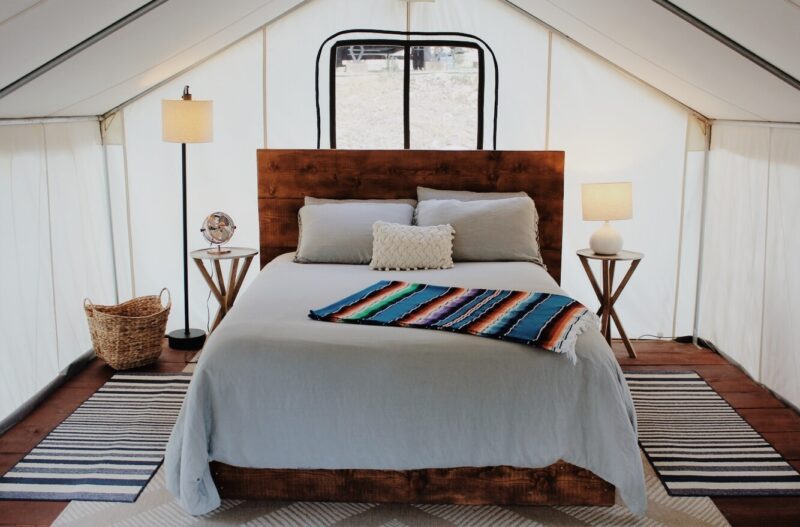 A large, well-appointed bed sits inside a well-lit tent.