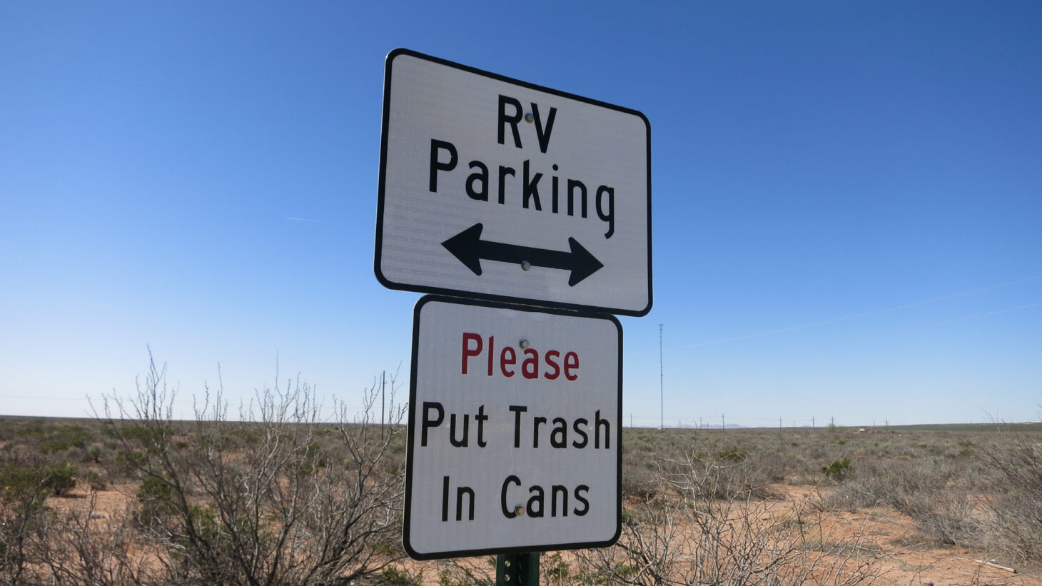 Sign at rest area reading "RV Parking" with two arrows and "Please Put Trash in Cans"