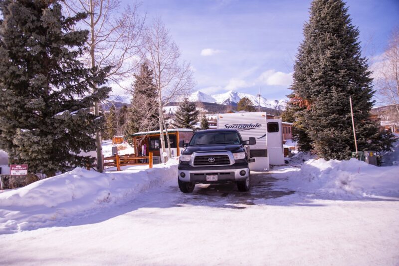 A snow-covered RV sits in a mountainous campground.
