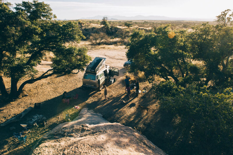 A drone captures a wide view of a quiet campsite tucked between trees on a dirt path.