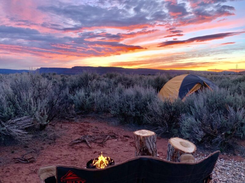 Camp chair setup in desert campground with tent overlooking sunset