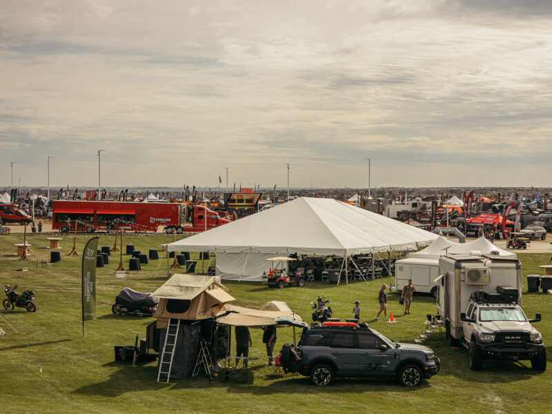 Large outdoor event with camping gear and a roof top tent set up near an SUV