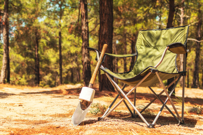 Camping chair with shovel and toilet paper in the woods. Outdoor camping equipment.