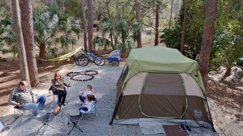 A family sits outside their tent at a Disney campsite where they have arranged pinecones in the shape of Mickey Mouse.