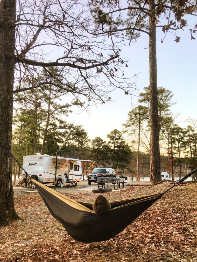 A hammock hangs between two trees as an RV is seen in the background