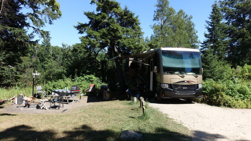 Large motorhome parked at a campsite surrounded by trees.