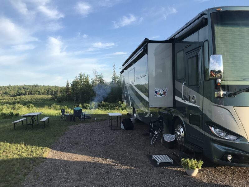 Large motorhome parked at a campsite with a slide extended and camping gear sitting outside
