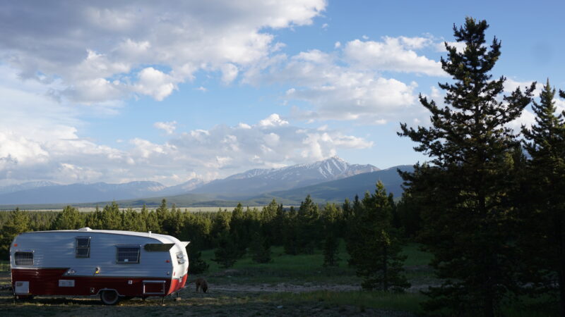 A retro red-and-white travel trailer sits in a remote camping spot with mountains in the distance