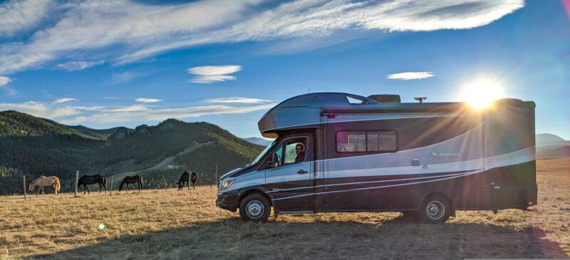 A Class C motorhome sits parked alongside horses in Wyoming