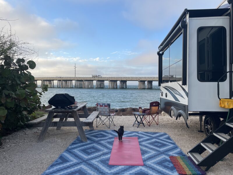 A sandy RV campsite sits right on the water's edge overlooking a bridge