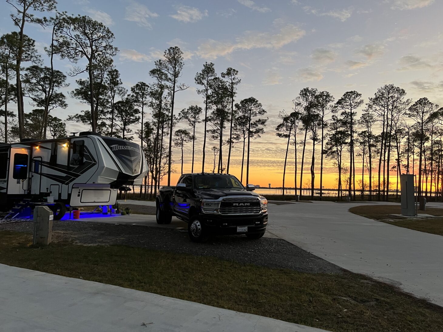Fifth wheel RV and pickup truck parked at a campsite with the sunsetting behind it