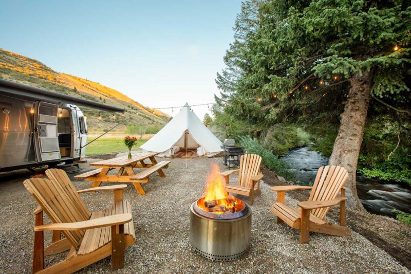 Airstream glamping setup with a tent, fire pit, and chairs