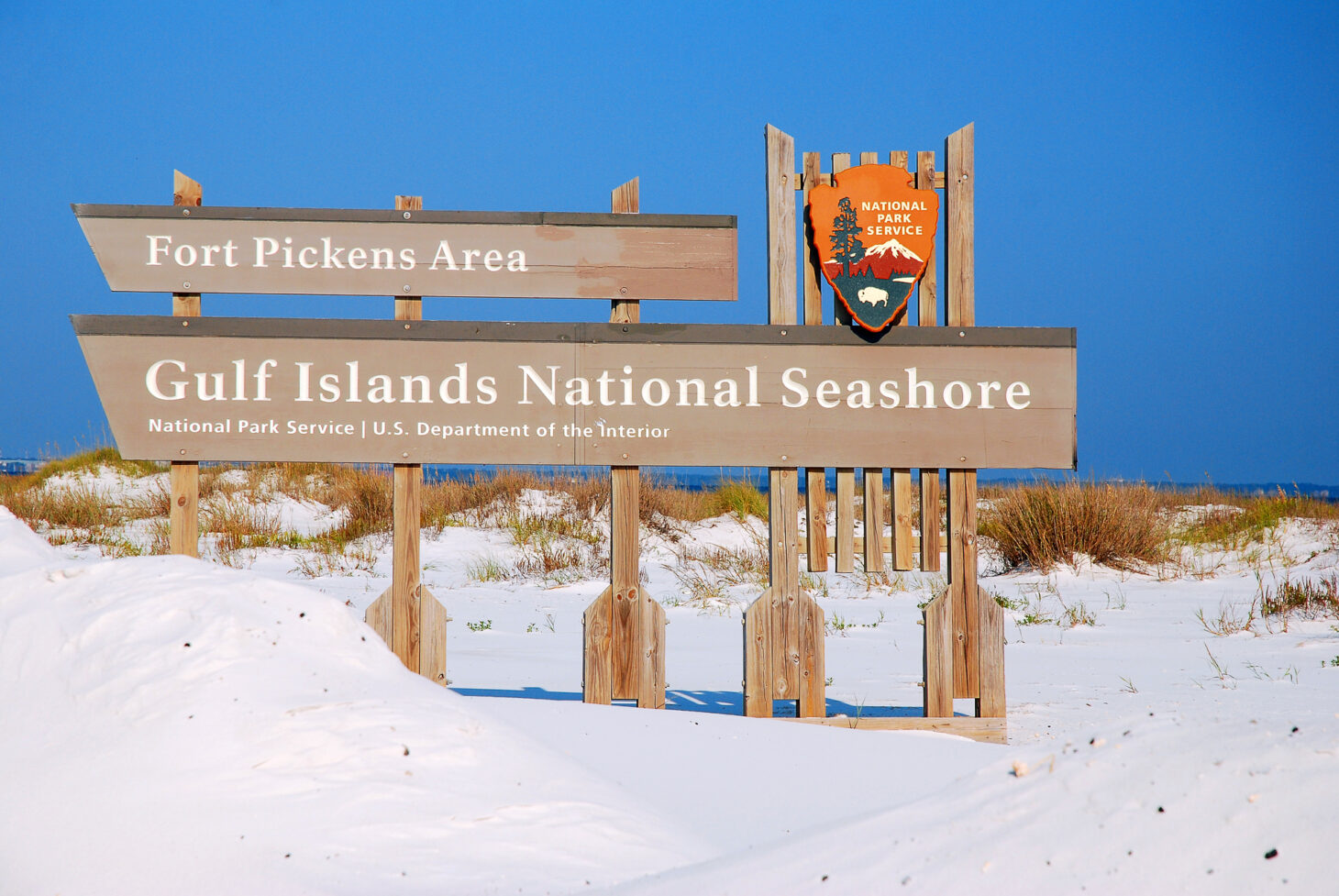 National Park Service sign that reads "Fort Pickens Area: Gulf Islands National Seashore" set in the sand at beach