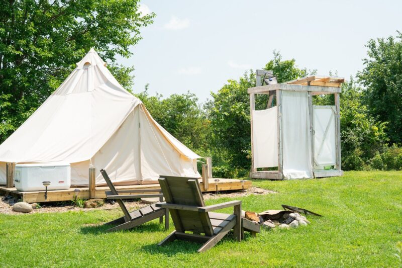 Exterior of a glamping tent, chairs, fire pit, and bath house