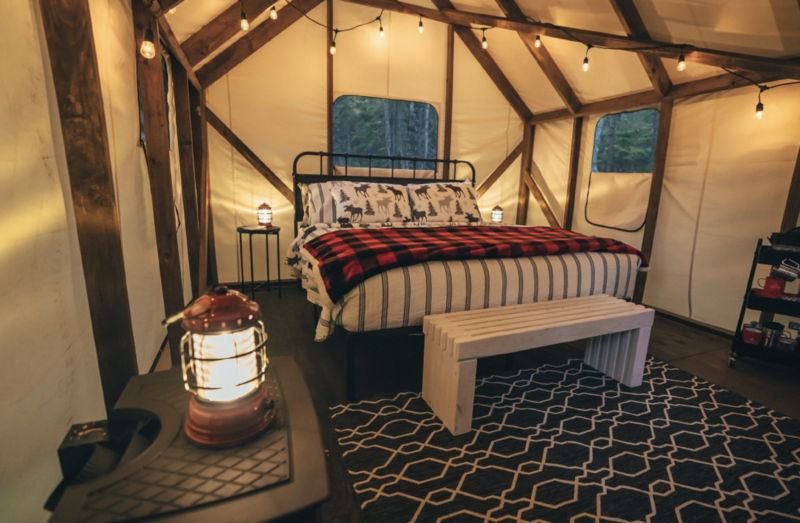 Interior of a glamping tent with a bed, lighting, and windows