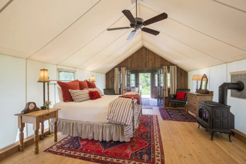 Interior of a glamping tent with a bed, ceiling fan, dressers, and wood floors