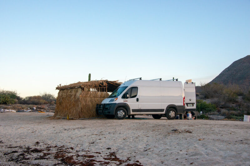 A small campervan sits on a rustic beach campsite