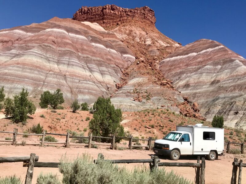 An RV sits parked alongside a towering red rock formation