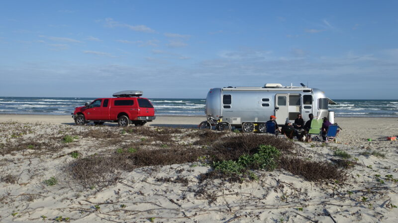Silver Airstream travel trailer parked on a beach with a red truck nearby