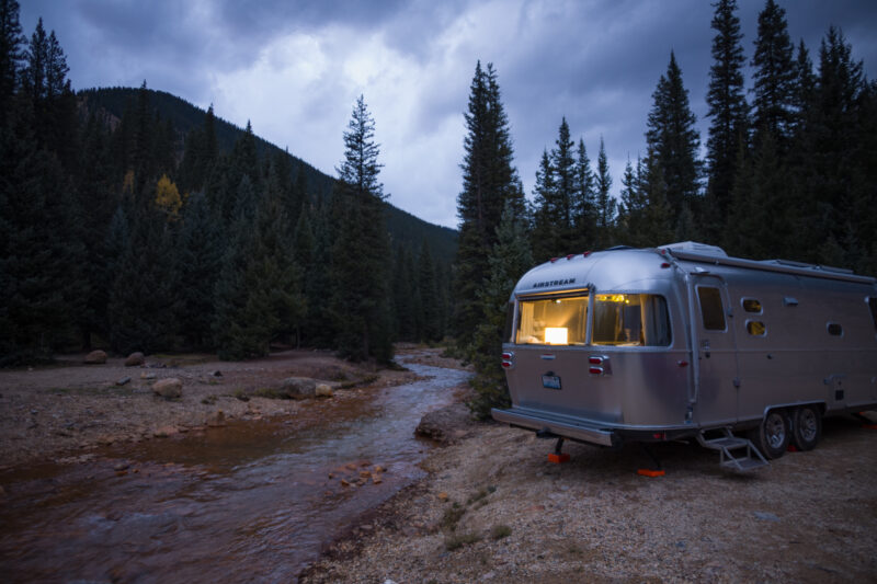 an airstream parked near a river bed surrounded by pine trees