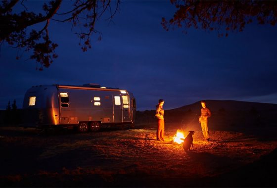 a couple hanging out by a campfire next to their airstream