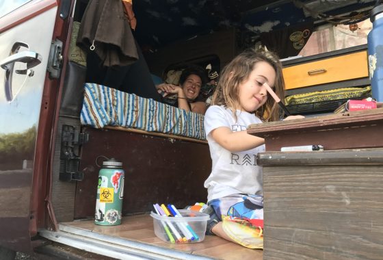 a woman lounges in her VW Bus, camping, while her son draws with markersa woman lounges in her VW Bus, camping, while her son draws with markers