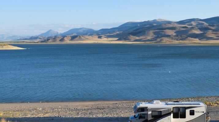 RV parked in front of a blue lake with mountains in the background