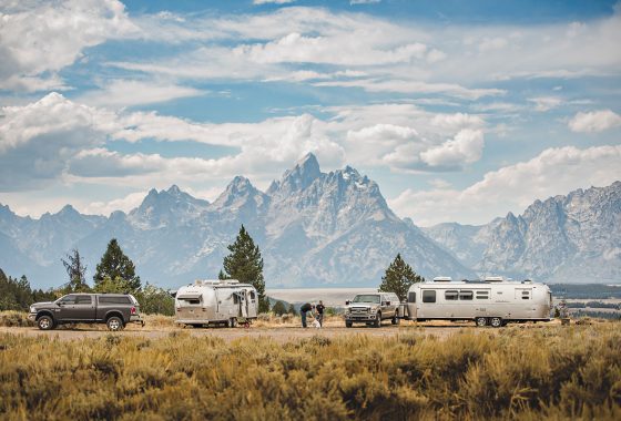 Two Airstreams parked in a field in front of the Teton Mountains.