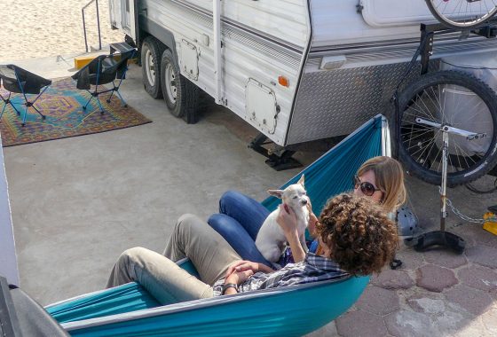 Couple and their dog sitting in a hammock outside their RV.