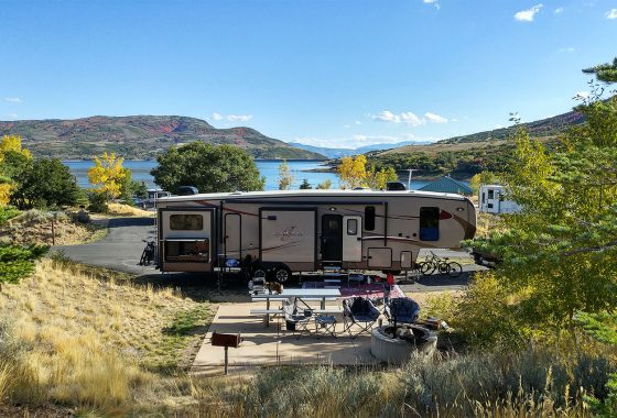 Fifth wheel surrounded by trees, mountains and a lake.