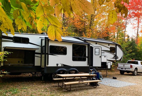 RV parked at a campground surrounded by fall colors.