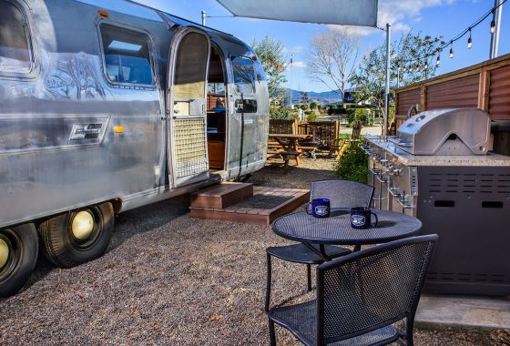 Airstream parked next to a outdoor grill and table.