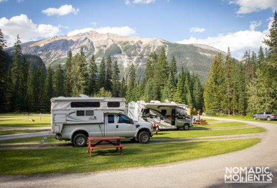 Multiple trailers at grassy campsite with rocky mountains in background