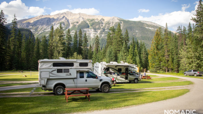 Multiple trailers at grassy campsite with rocky mountains in background