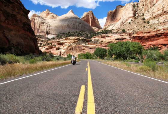 Motorcyclist riding on empty road surrounded by red rocks