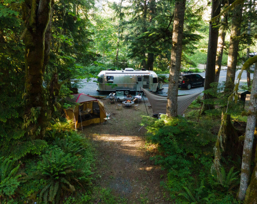 a campsite with an airstream, tent and hammock in the woods